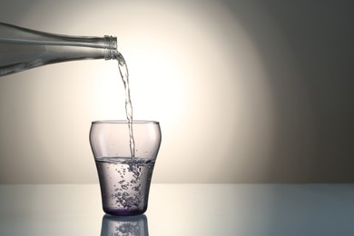 Photo of Pouring water from bottle into glass on mirror table against gray gradient background, space for text