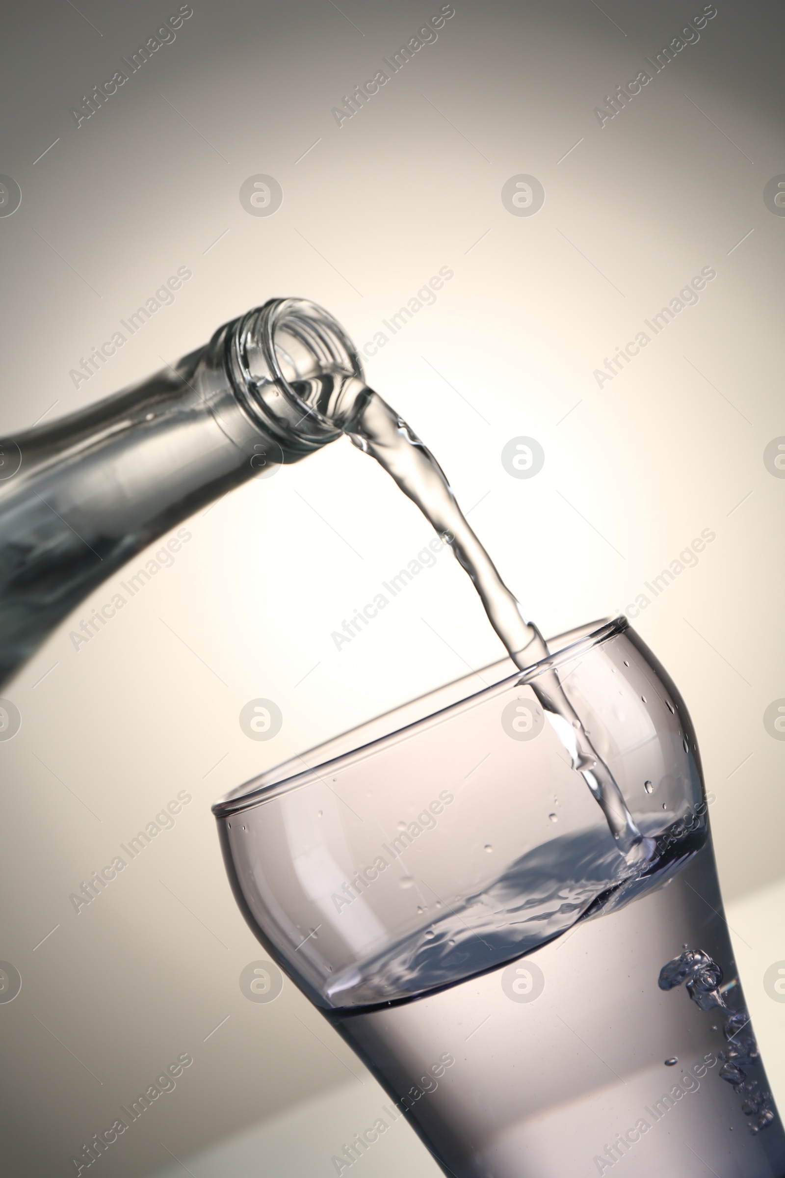 Photo of Pouring water from bottle into glass on gray gradient background, closeup