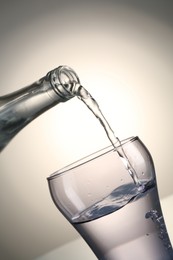 Photo of Pouring water from bottle into glass on gray gradient background, closeup