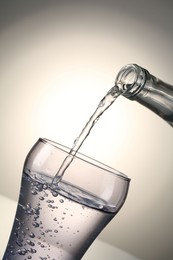 Photo of Pouring water from bottle into glass on gray gradient background, closeup