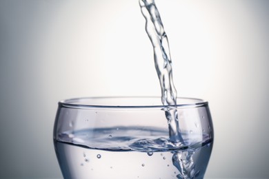 Photo of Pouring water into glass on gray gradient background, closeup