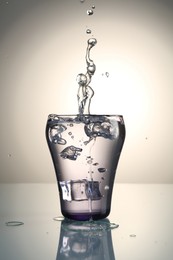 Photo of Fresh water splashing out of glass on mirror table against gray gradient background