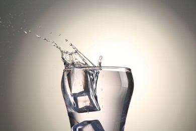 Photo of Fresh water splashing out of glass on gray gradient background, closeup