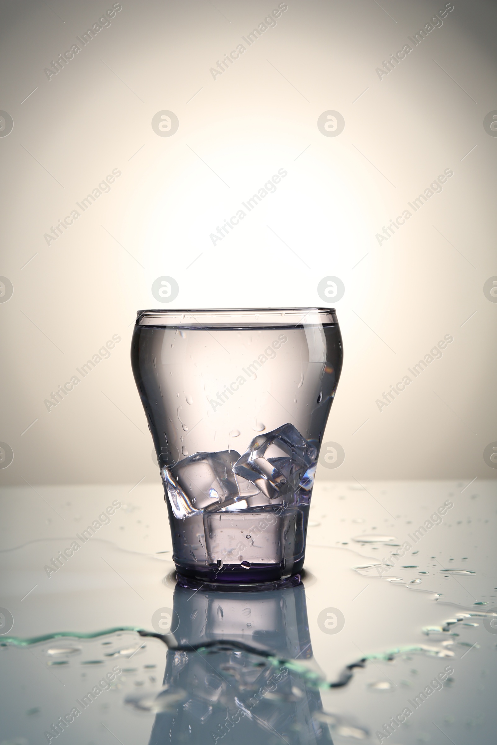 Fresh water with ice cubes in glass on mirror table against gray gradient background Photo of Fresh water with ice cubes in glass on mirror table against gray gradient background