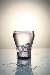 Photo of Fresh water with ice cubes in glass on mirror table against gray gradient background