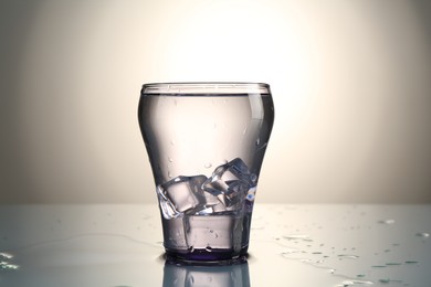 Photo of Fresh water with ice cubes in glass on mirror table against gray gradient background