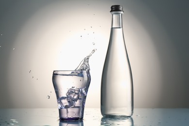 Photo of Fresh water splashing out of glass on mirror table against gray gradient background