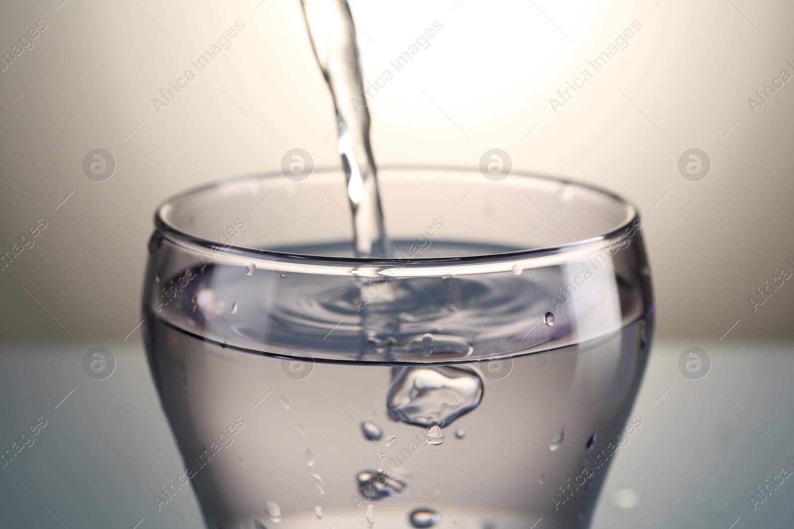 Photo of Pouring water into glass on gray gradient background, closeup