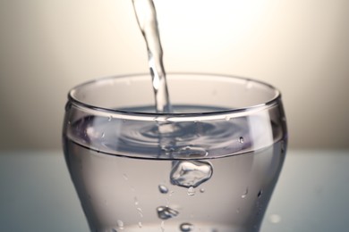 Photo of Pouring water into glass on gray gradient background, closeup