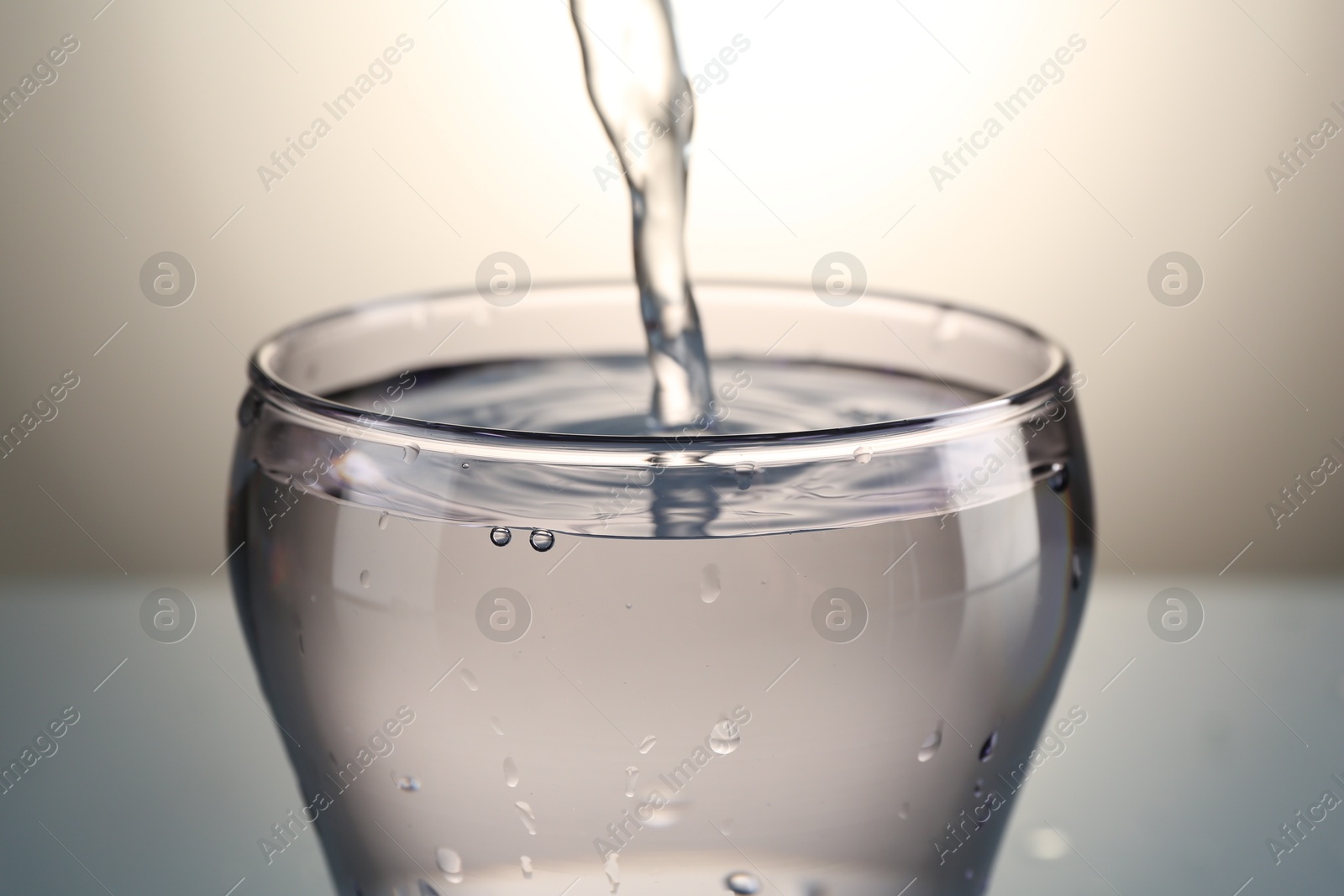 Pouring water into glass on gray gradient background, closeup Photo of Pouring water into glass on gray gradient background, closeup