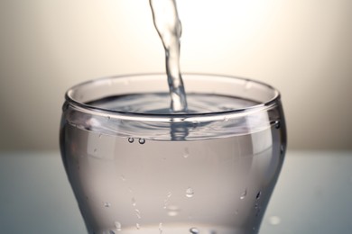 Photo of Pouring water into glass on gray gradient background, closeup