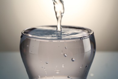 Photo of Pouring water into glass on gray gradient background, closeup