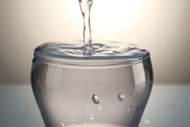 Photo of Pouring water into glass on gray gradient background, closeup