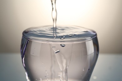 Photo of Pouring water into glass on gray gradient background, closeup