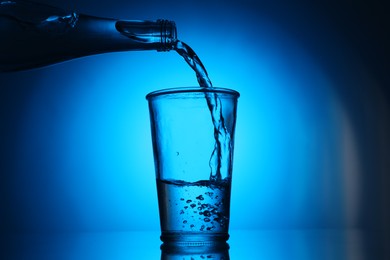 Photo of Pouring water from bottle into glass on blue gradient background. Backlit