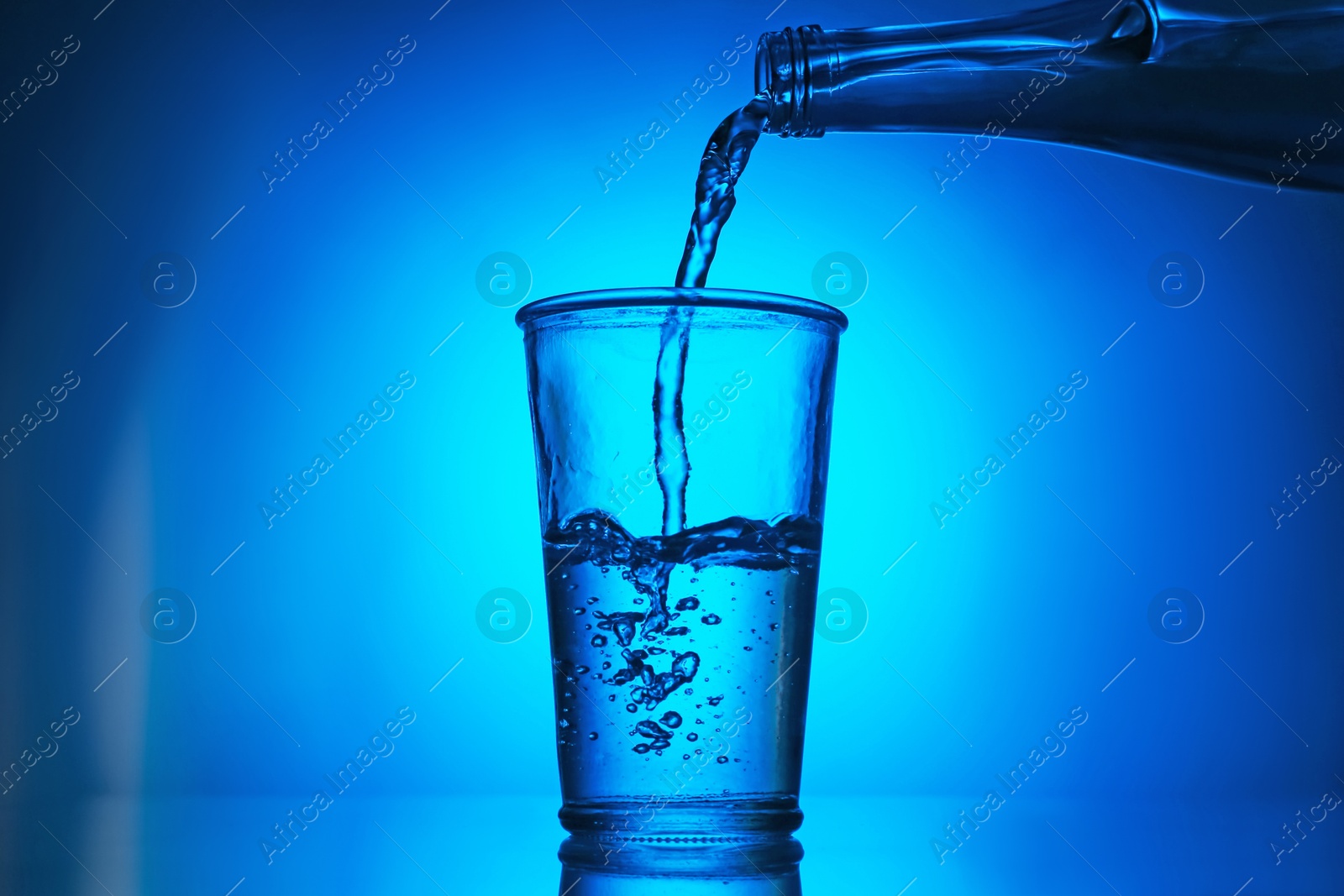 Pouring water from bottle into glass on blue gradient background. Backlit Photo of Pouring water from bottle into glass on blue gradient background. Backlit