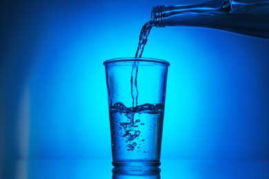 Photo of Pouring water from bottle into glass on blue gradient background. Backlit