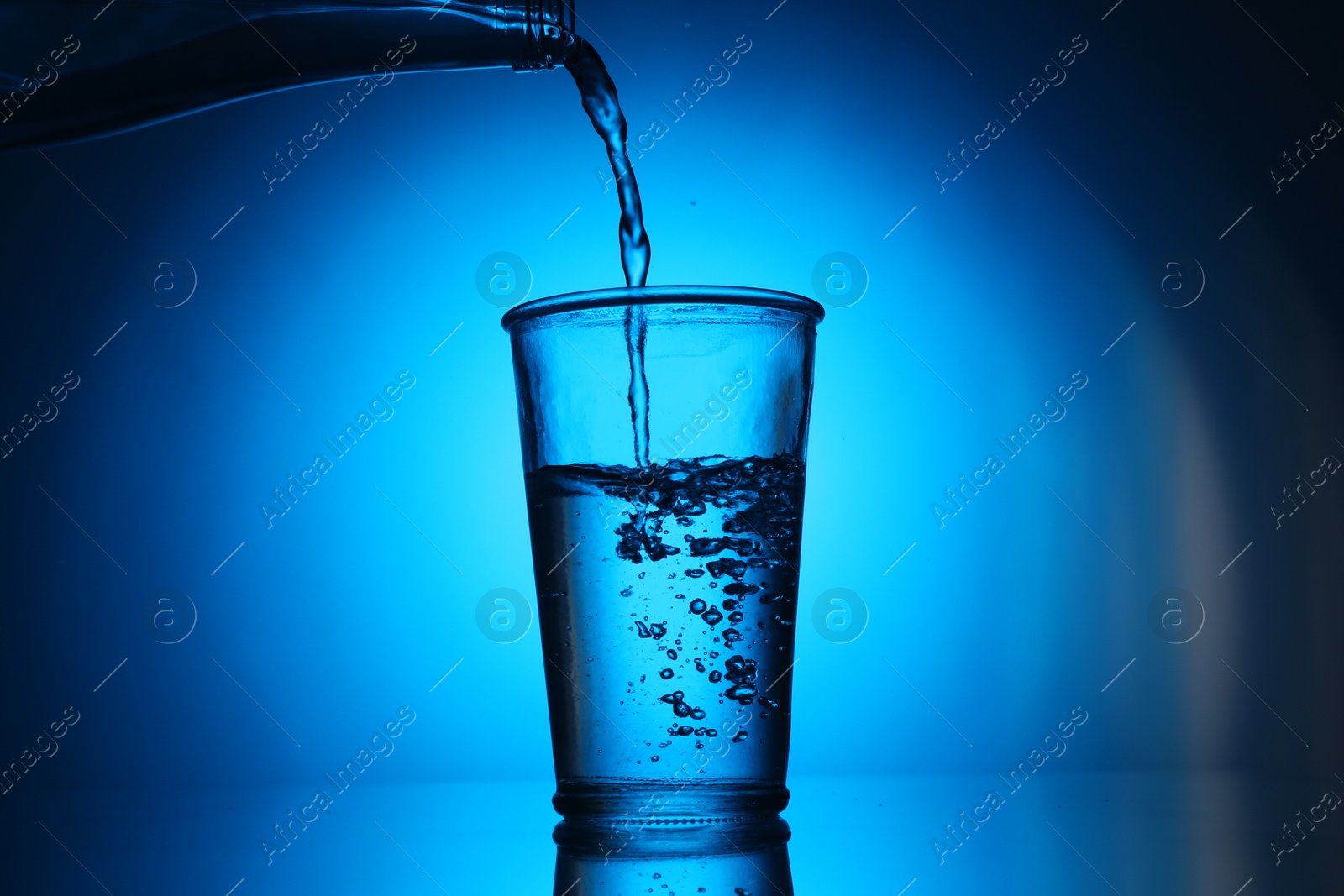 Pouring water from bottle into glass on blue gradient background. Backlit Photo of Pouring water from bottle into glass on blue gradient background. Backlit