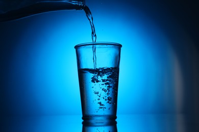 Photo of Pouring water from bottle into glass on blue gradient background. Backlit