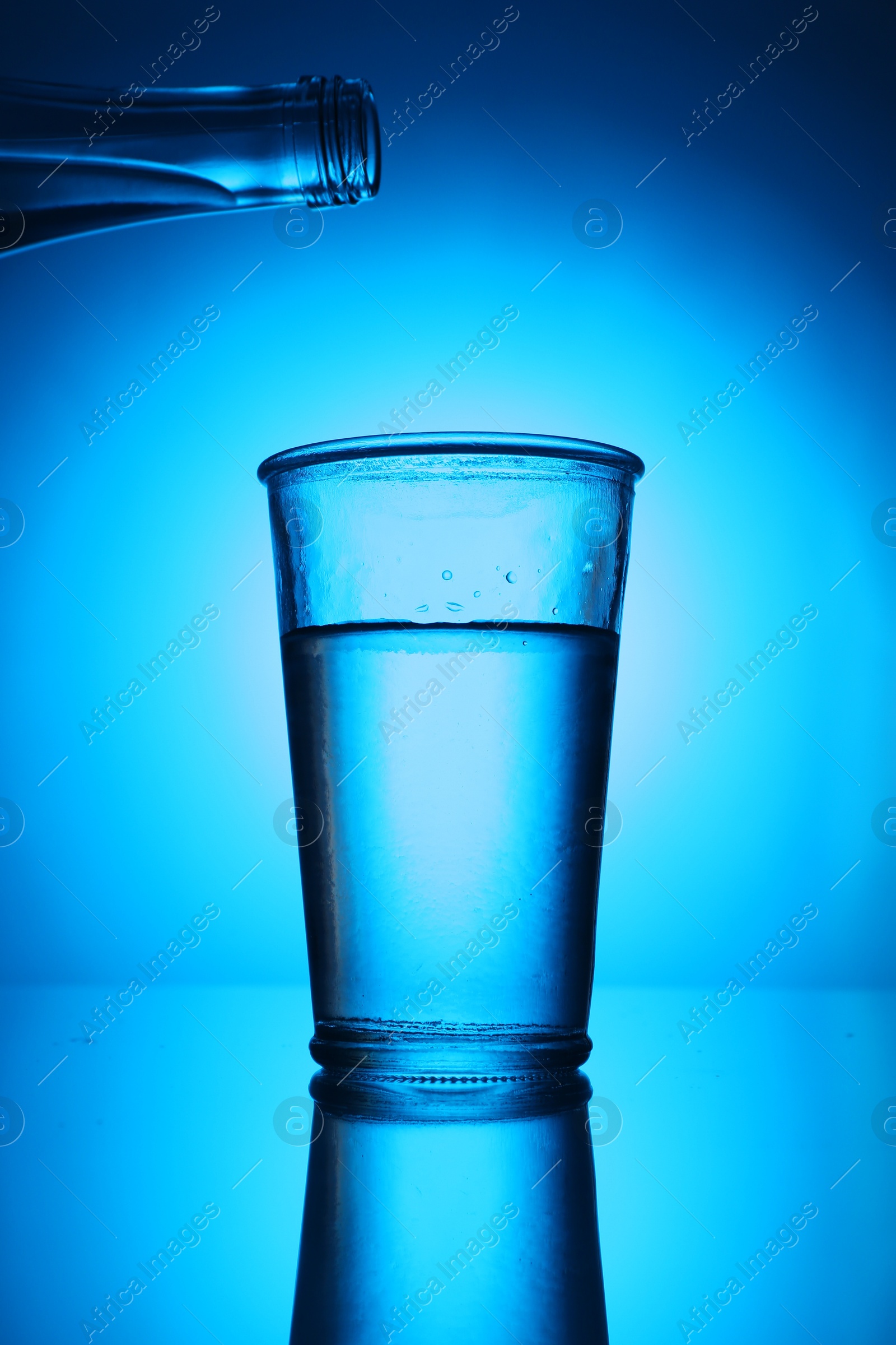 Bottle above glass of fresh water on blue gradient background. Backlit Photo of Bottle above glass of fresh water on blue gradient background. Backlit