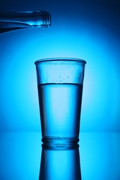 Photo of Bottle above glass of fresh water on blue gradient background. Backlit