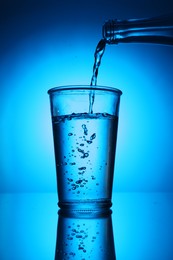 Photo of Pouring water from bottle into glass on blue gradient background. Backlit