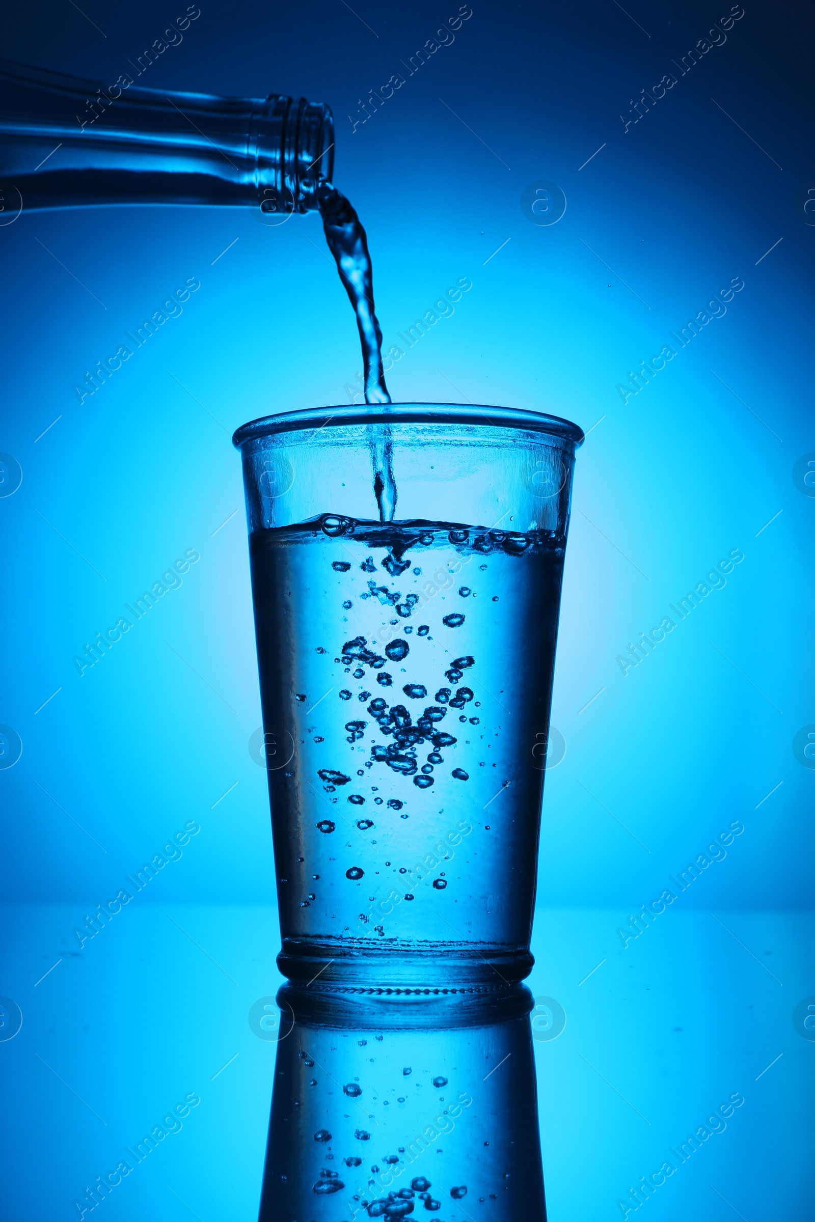 Pouring water from bottle into glass on blue gradient background. Backlit Photo of Pouring water from bottle into glass on blue gradient background. Backlit