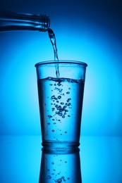 Photo of Pouring water from bottle into glass on blue gradient background. Backlit