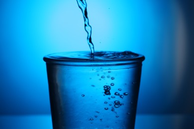 Photo of Pouring water into glass on blue gradient background, closeup. Backlit