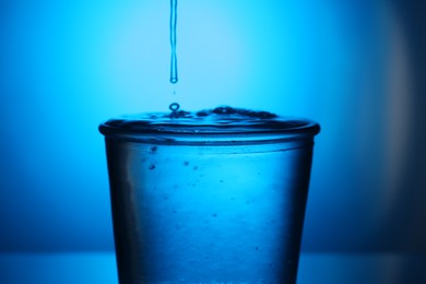 Photo of Fresh water in glass on blue gradient background, closeup. Backlit