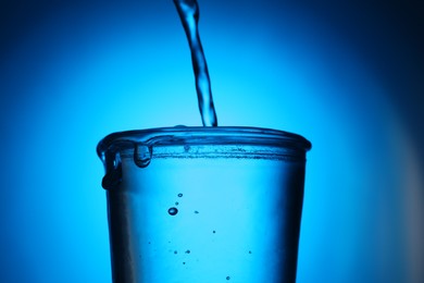 Photo of Pouring water into glass on blue gradient background, closeup. Backlit