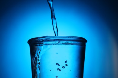 Photo of Pouring water into glass on blue gradient background, closeup. Backlit