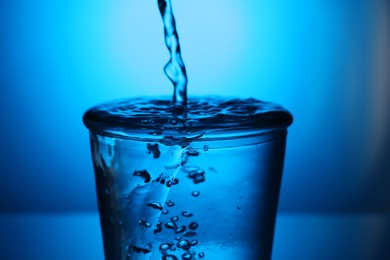 Photo of Pouring water into glass on blue gradient background, closeup. Backlit