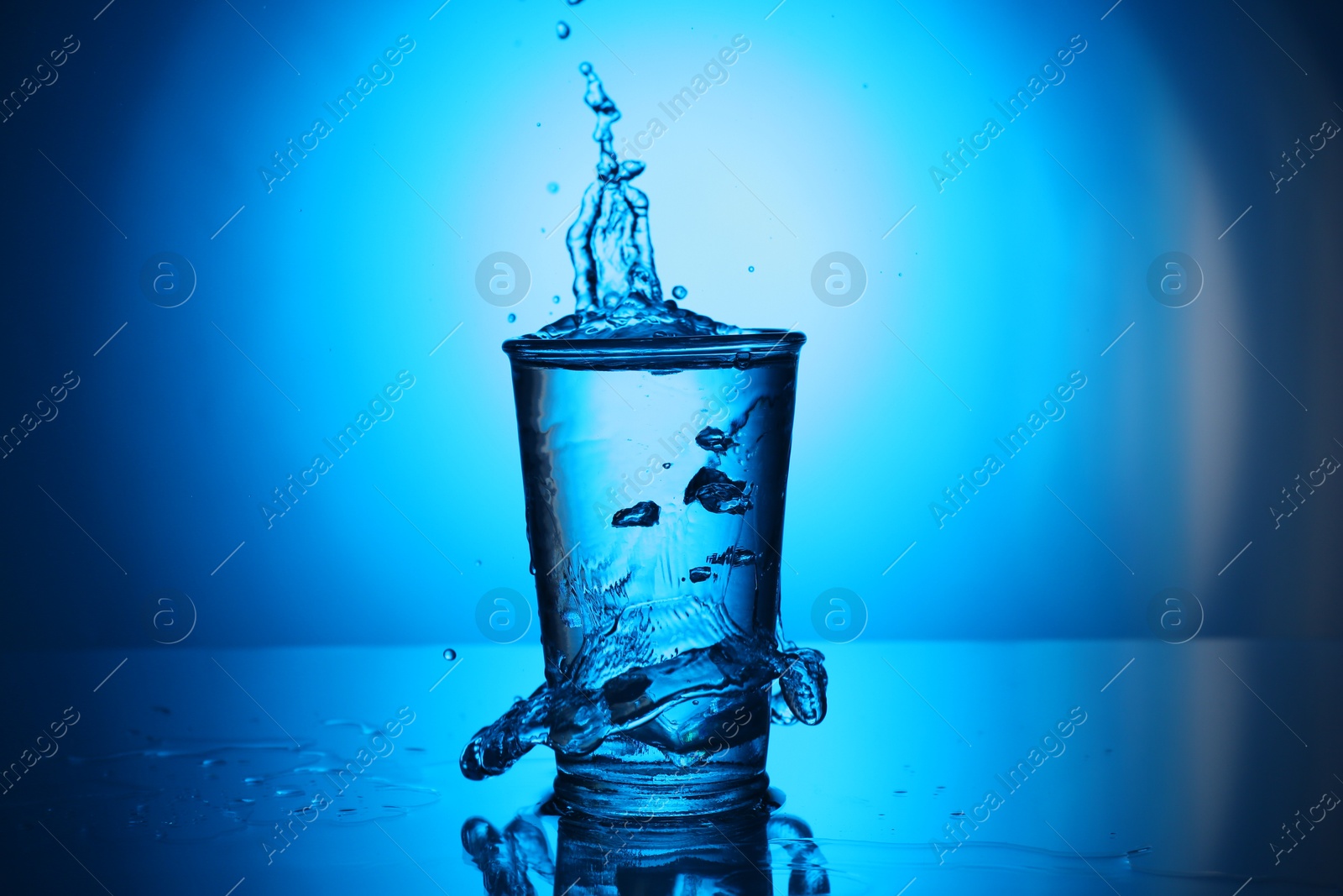 Fresh water overflowing from glass on blue gradient background. Backlit Photo of Fresh water overflowing from glass on blue gradient background. Backlit