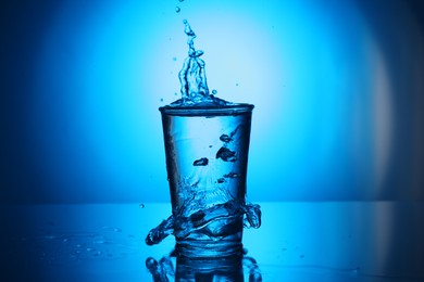 Photo of Fresh water overflowing from glass on blue gradient background. Backlit