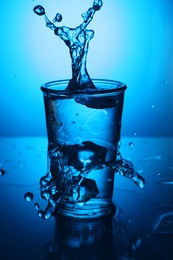 Photo of Fresh water splashing out of glass on blue gradient background. Backlit