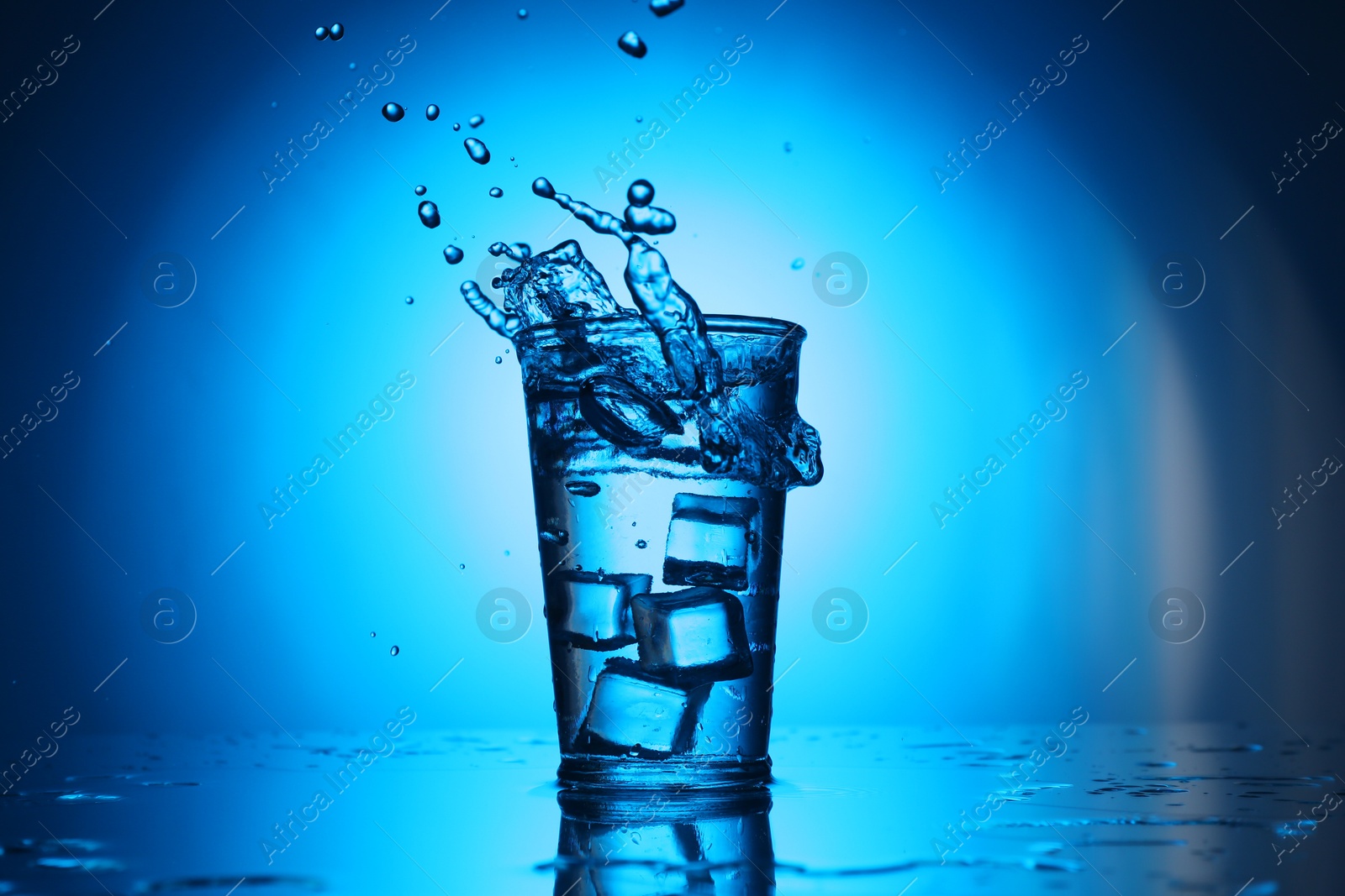 Fresh water splashing out of glass on blue gradient background. Backlit Photo of Fresh water splashing out of glass on blue gradient background. Backlit