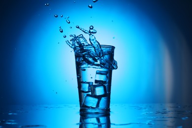 Photo of Fresh water splashing out of glass on blue gradient background. Backlit