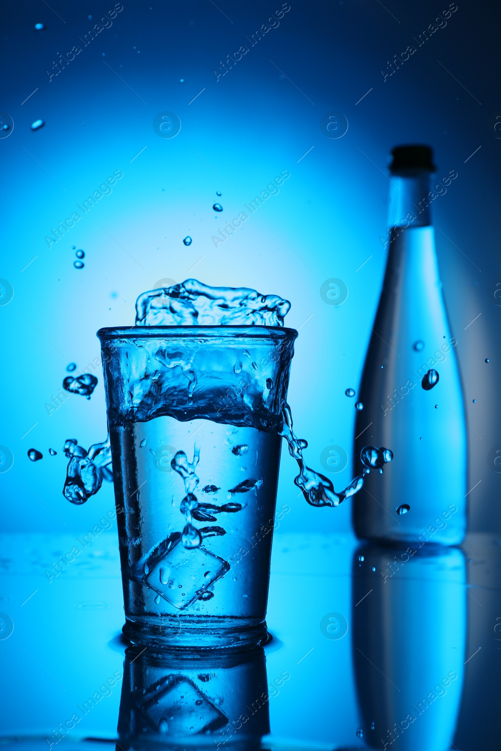Fresh water splashing out of glass on blue gradient background. Backlit Photo of Fresh water splashing out of glass on blue gradient background. Backlit
