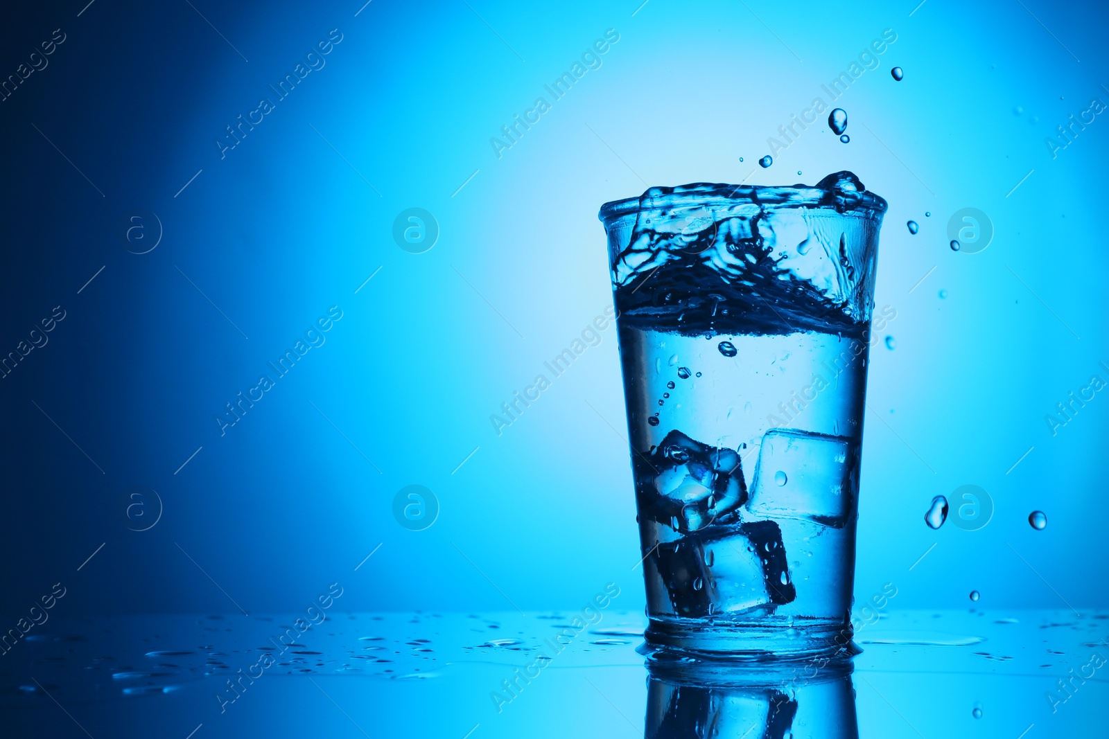Photo of Fresh water splashing out of glass on blue gradient background, space for text. Backlit