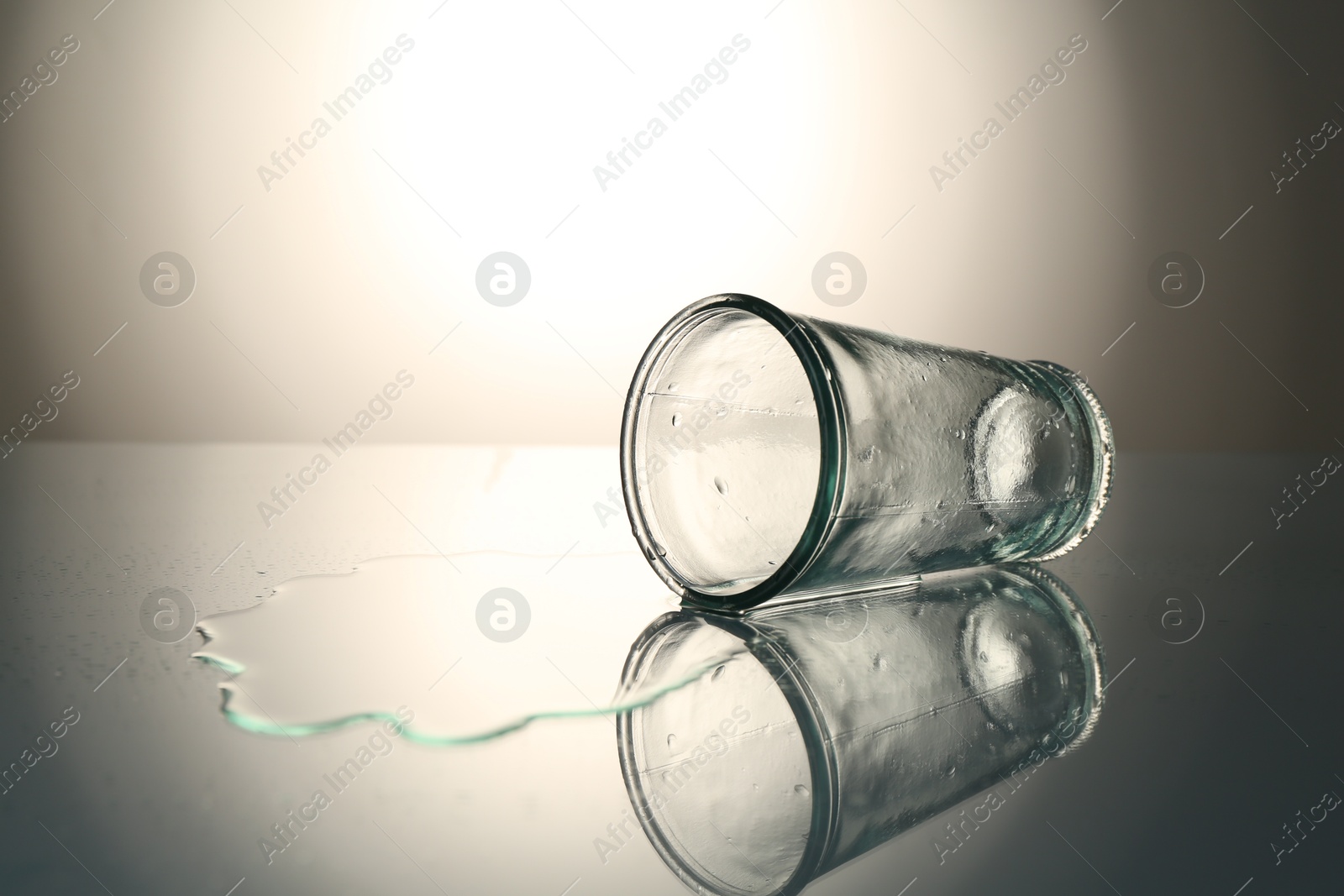 Overturned glass and spilled water on mirror table against gray gradient background, space for text Photo of Overturned glass and spilled water on mirror table against gray gradient background, space for text