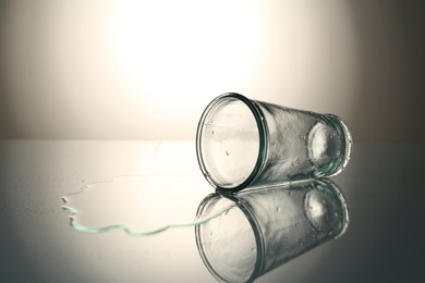 Photo of Overturned glass and spilled water on mirror table against gray gradient background, space for text