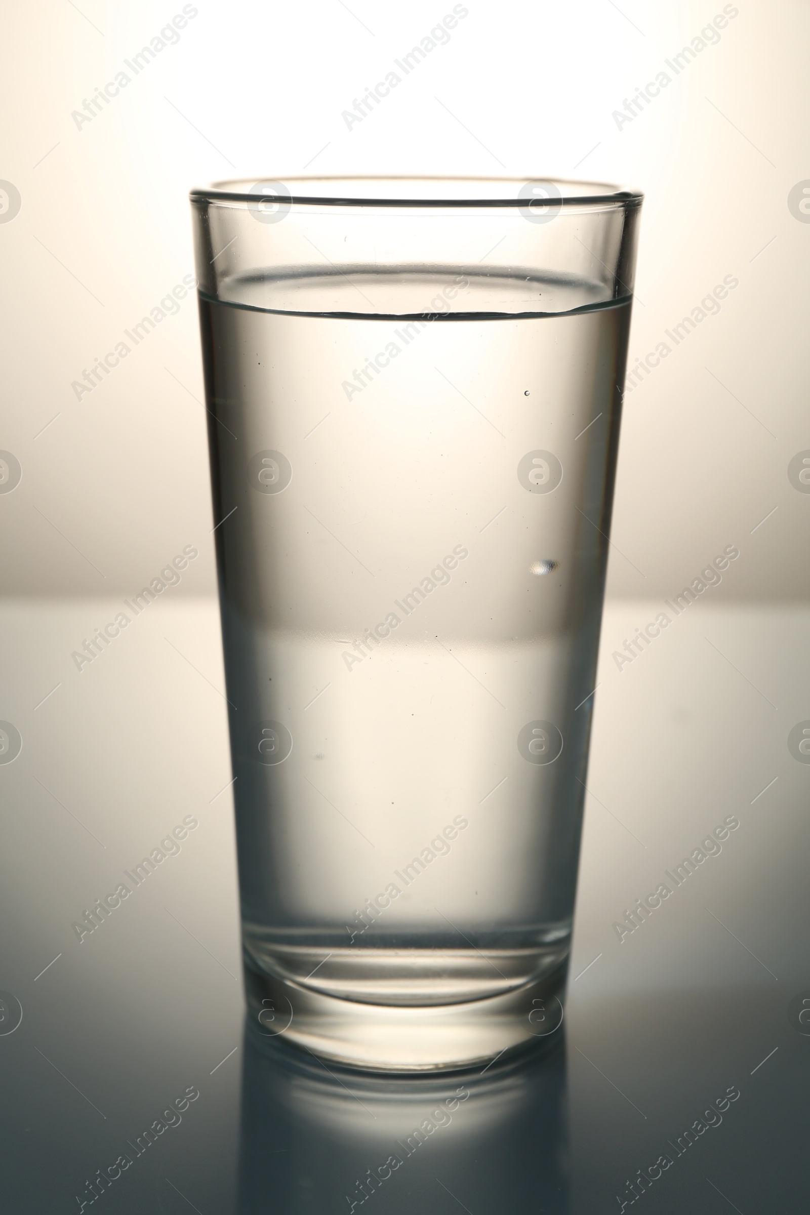 Fresh water in glass on mirror table against gray gradient background Photo of Fresh water in glass on mirror table against gray gradient background