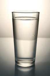 Photo of Fresh water in glass on mirror table against gray gradient background