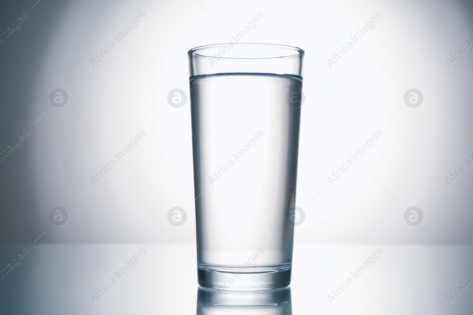 Fresh water in glass on mirror table against gray gradient background Photo of Fresh water in glass on mirror table against gray gradient background