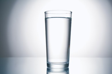 Photo of Fresh water in glass on mirror table against gray gradient background