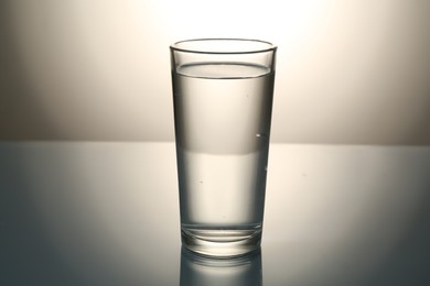 Photo of Fresh water in glass on mirror table against gray gradient background