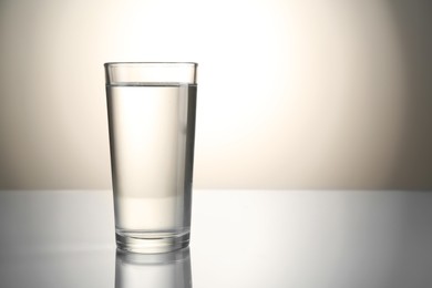 Photo of Fresh water in glass on mirror table against gray gradient background, space for text