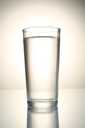 Photo of Fresh water in glass on mirror table against gray gradient background