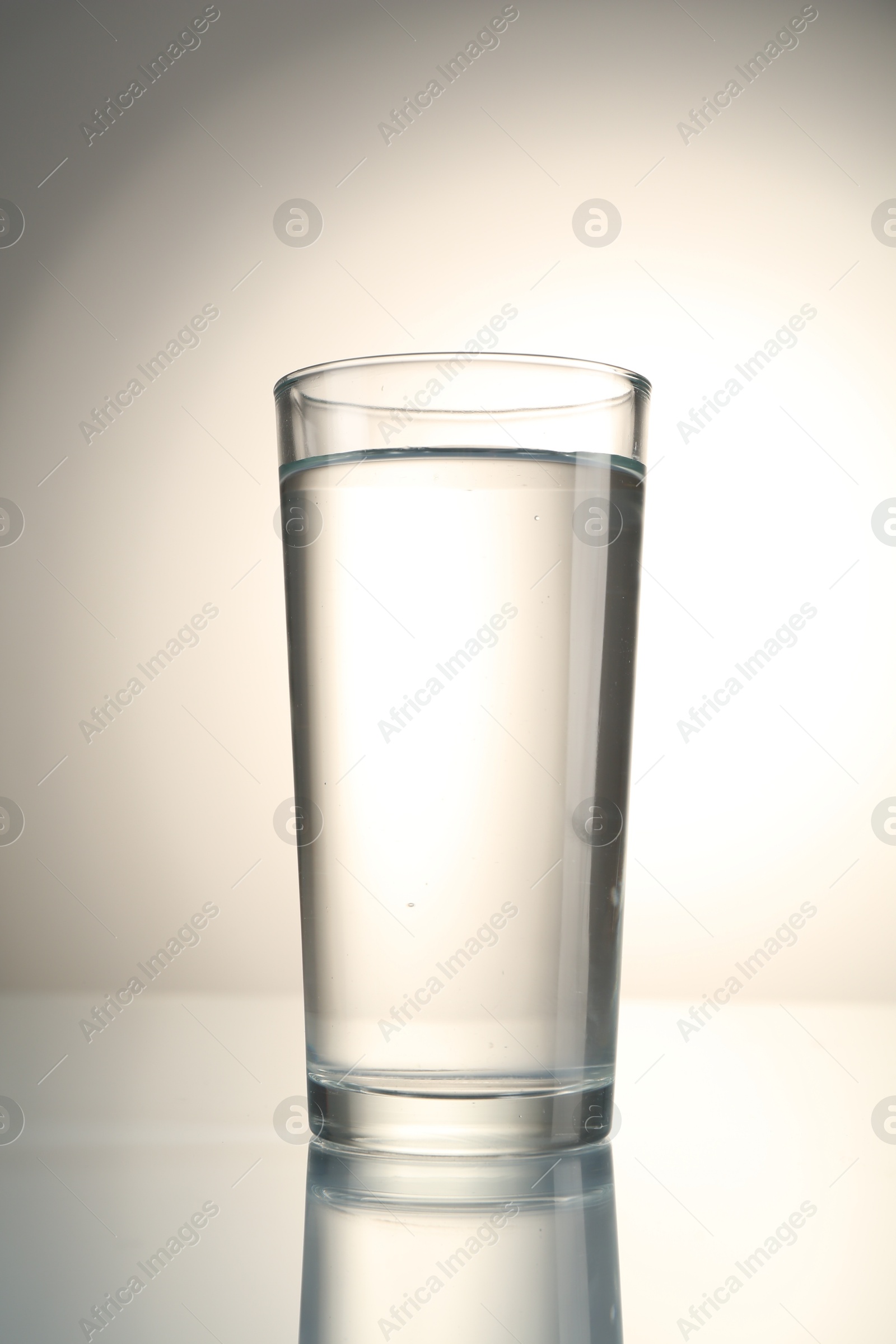 Photo of Fresh water in glass on mirror table against gray gradient background